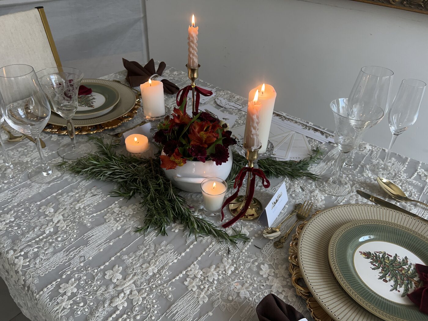 Mesa de Natal em construção: velas de alturas diferentes, guirlanda de alecrim e pratos sendo posicionados